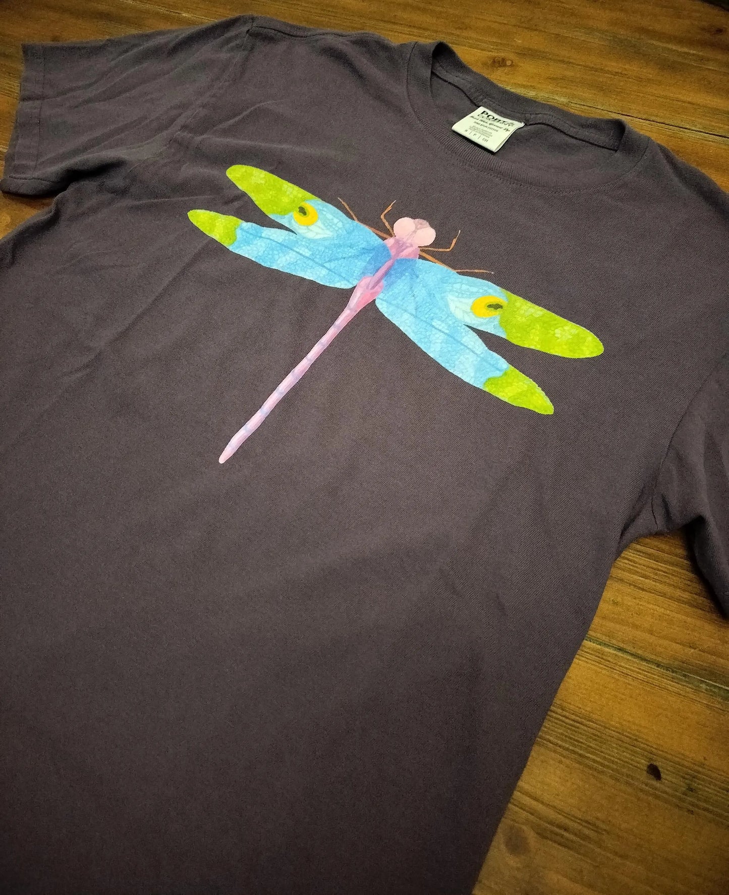 purple t-shirt with a colorful dragonfly design on a wooden surface