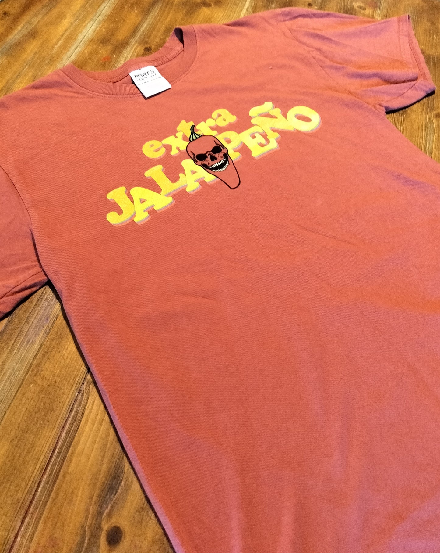 Red t-shirt with yellow text and a skull graphic on a wooden surface