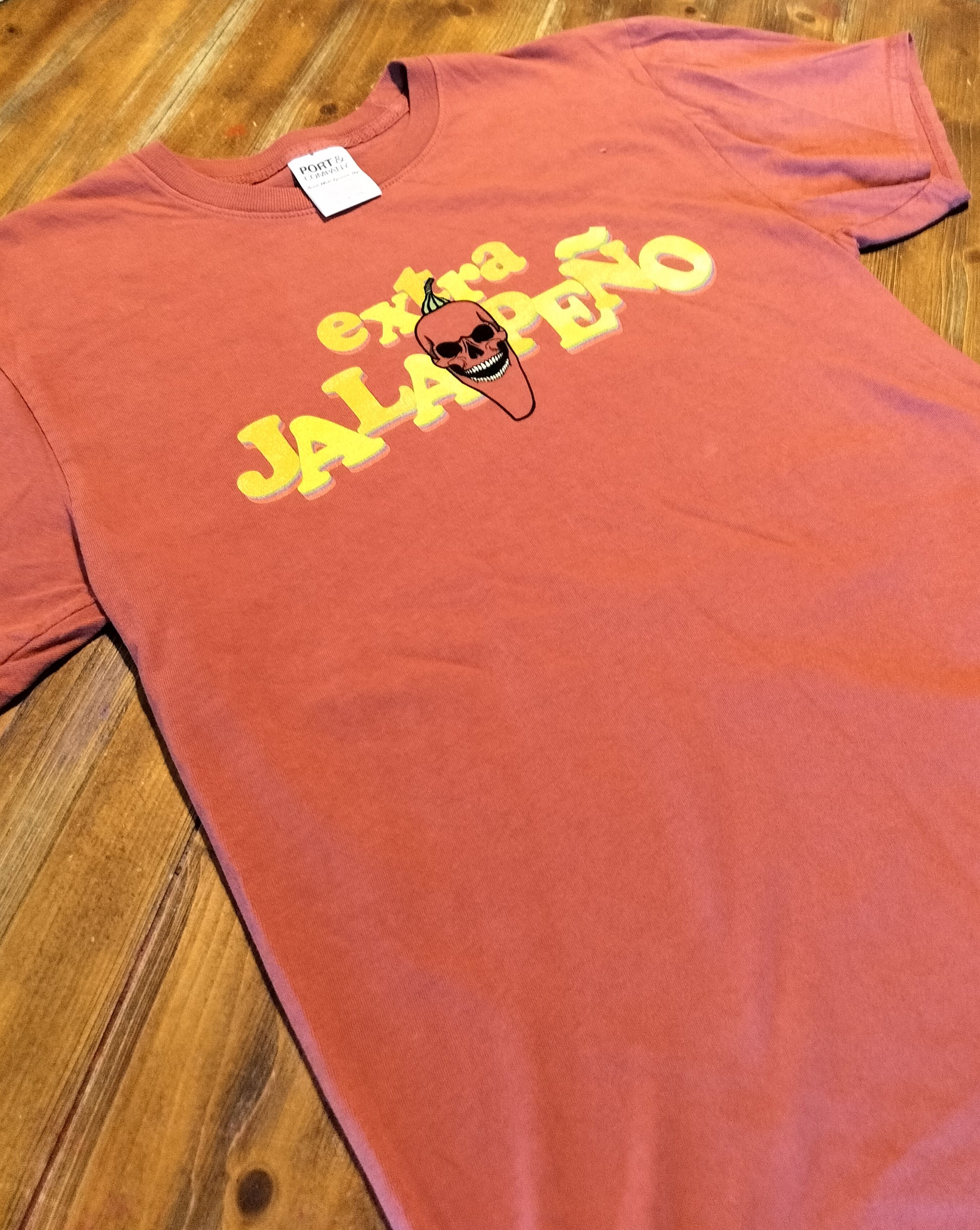 Red t-shirt with yellow text and a skull graphic on a wooden surface