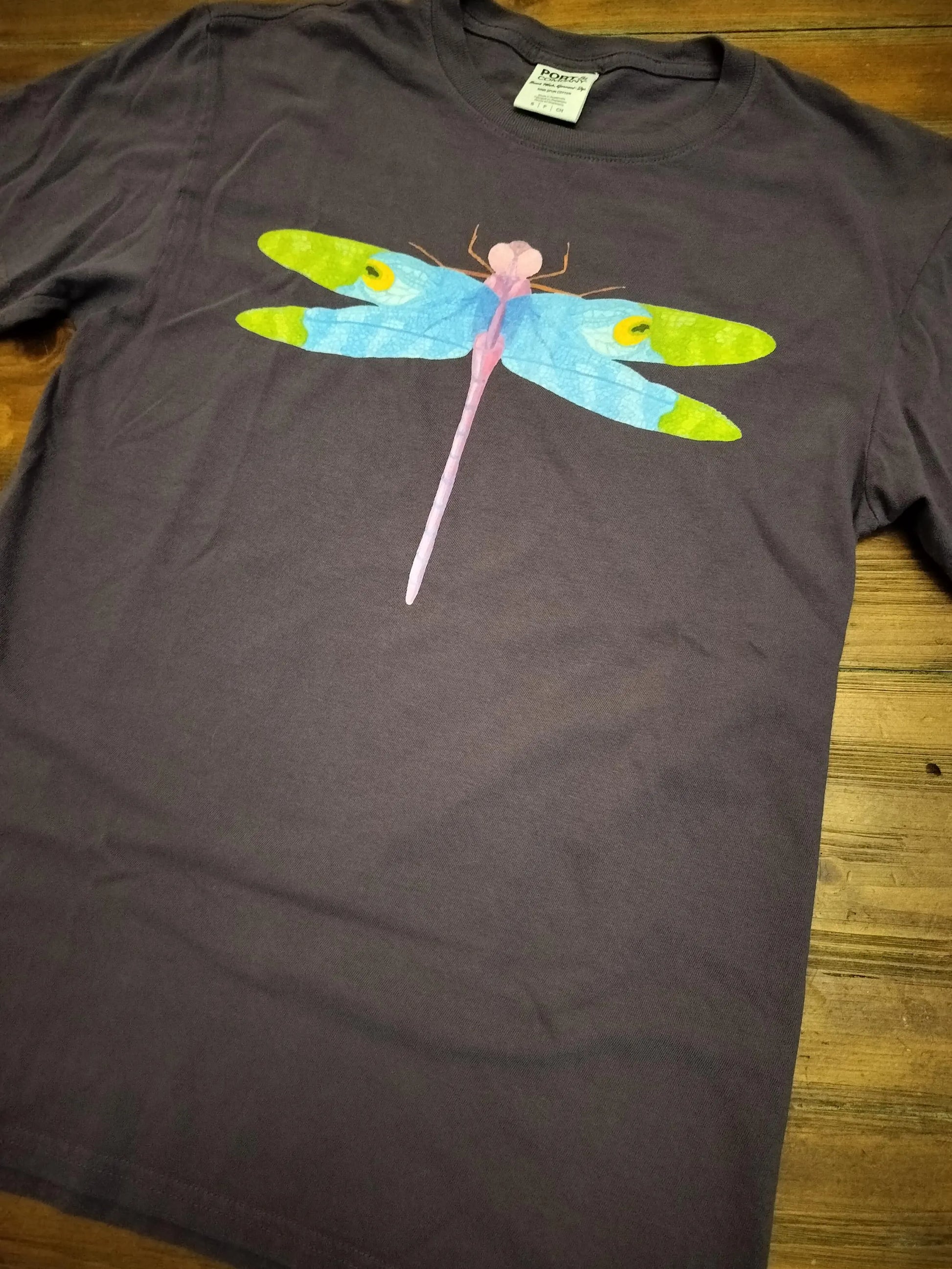 Purple t-shirt with a colorful dragonfly design on a wooden surface