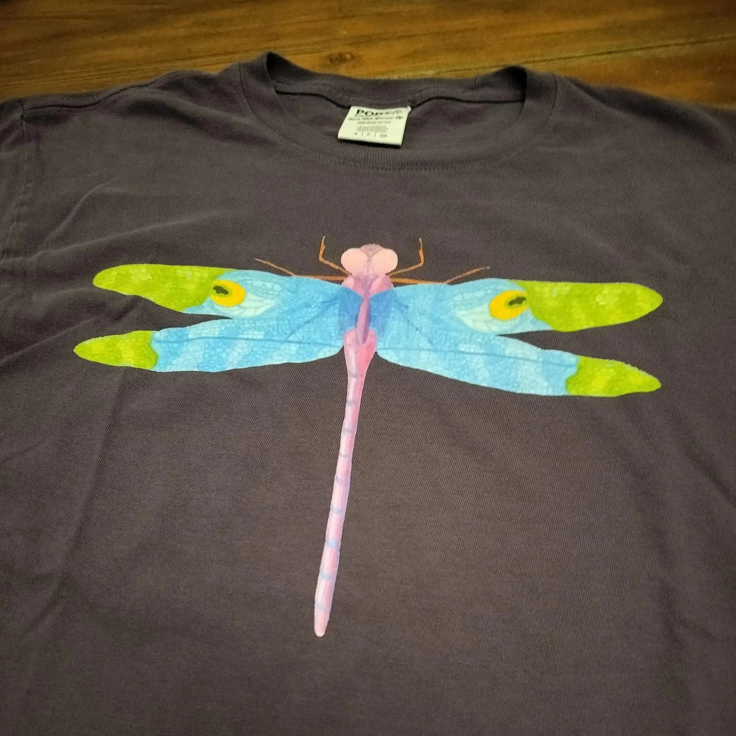 Purple t-shirt with a colorful dragonfly design on a wooden surface