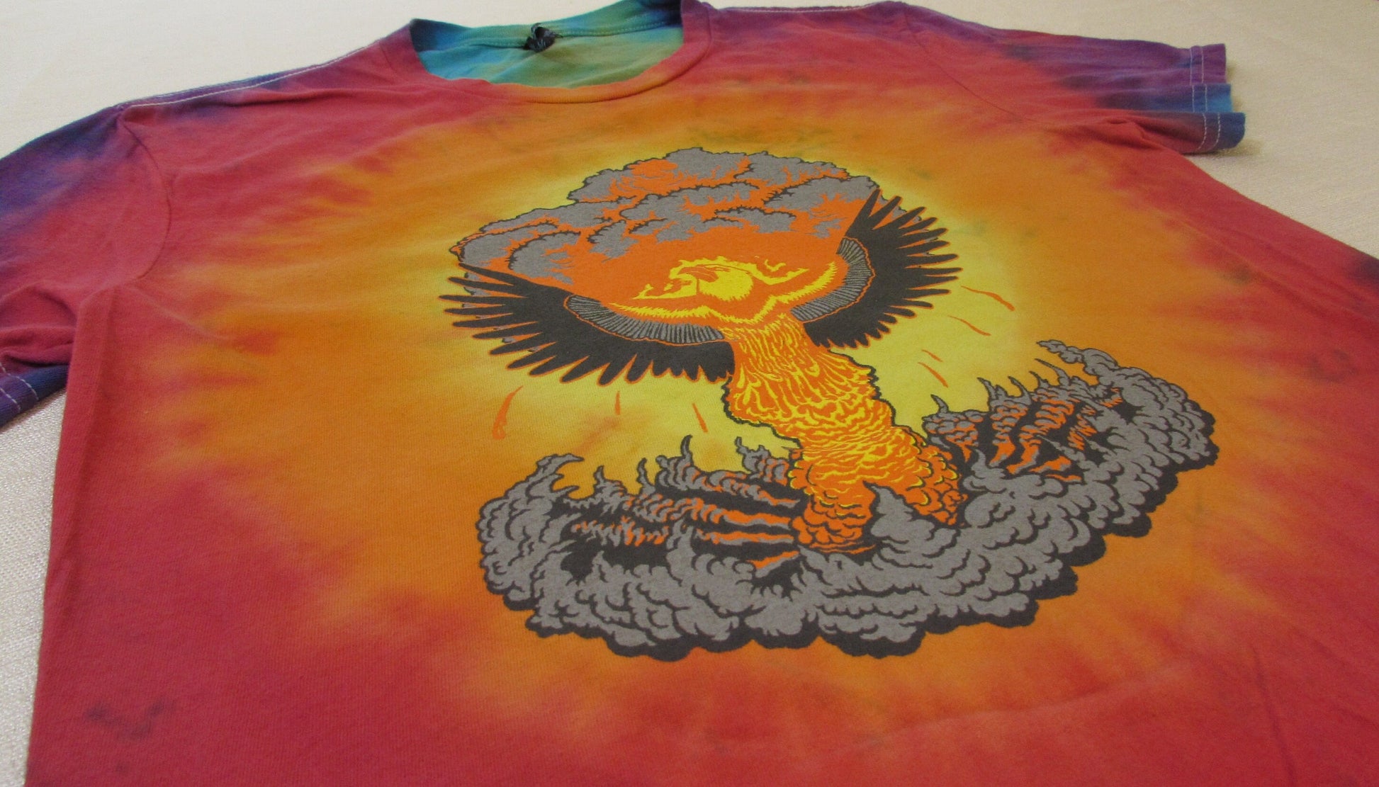 Phoenix rising out of a mushroom cloud on a tie dye shirt with a white background