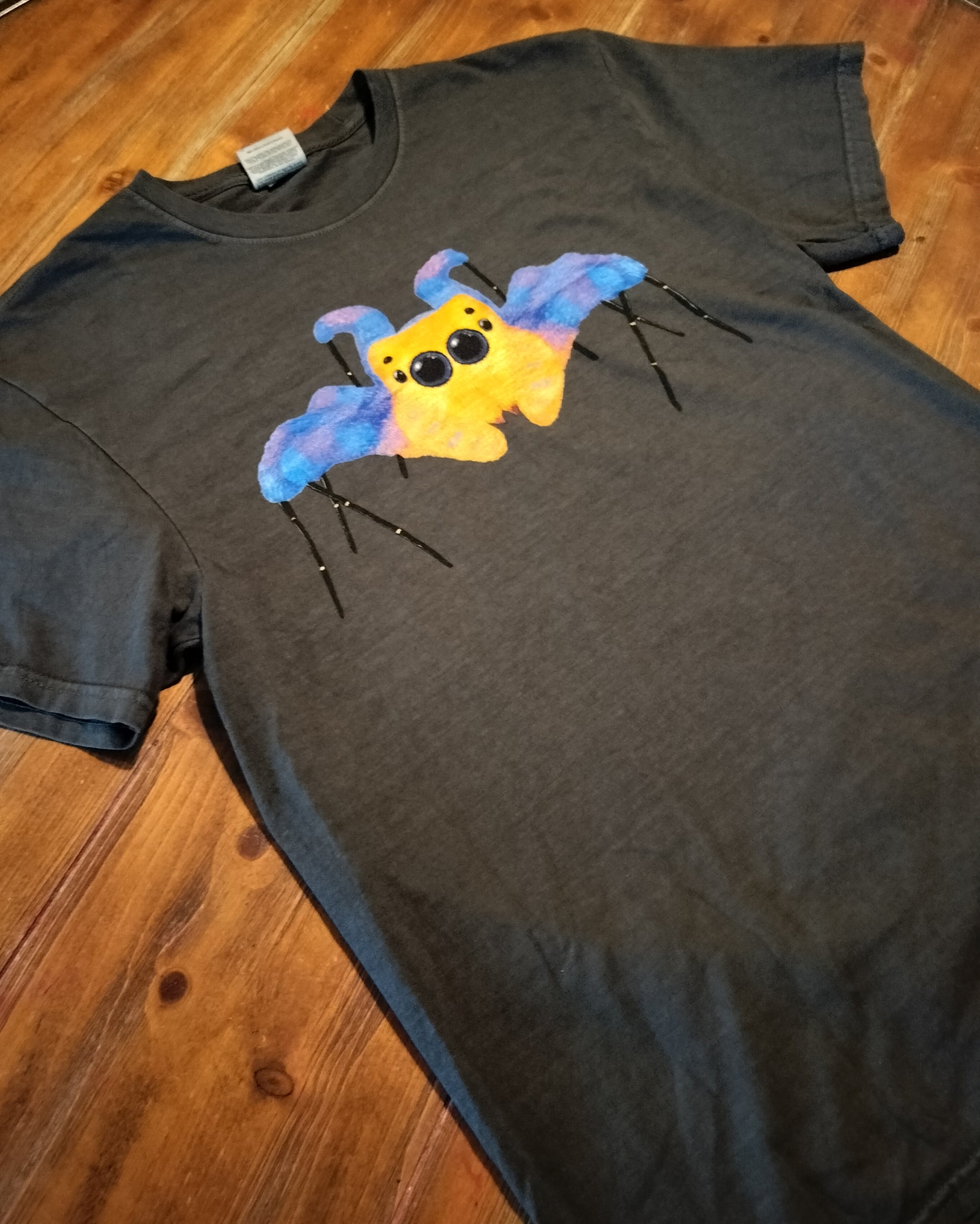 Grey t-shirt with a colorful Jumping spider design on a wooden background