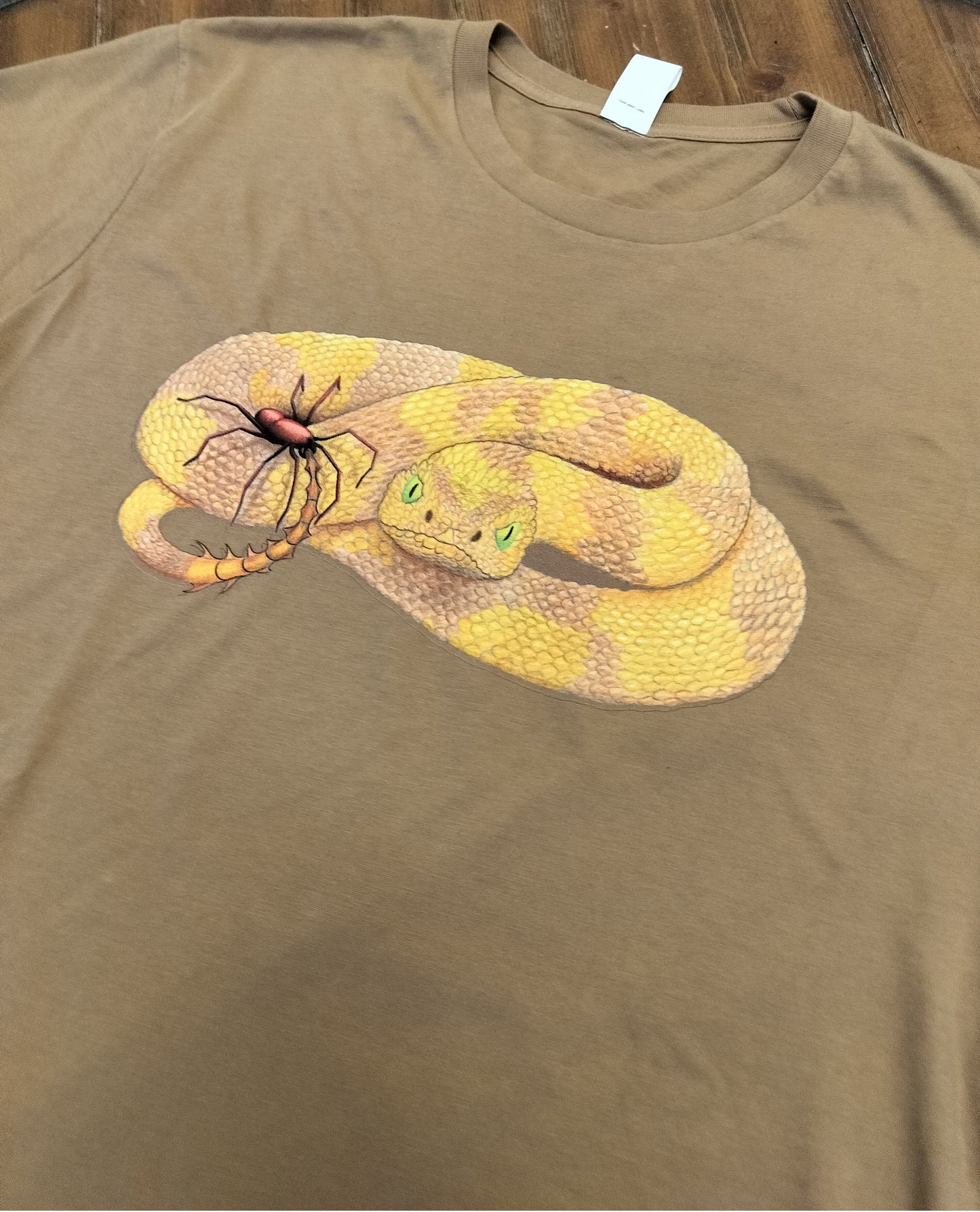 Brown t-shirt with a snake and spider graphic on a wooden surface