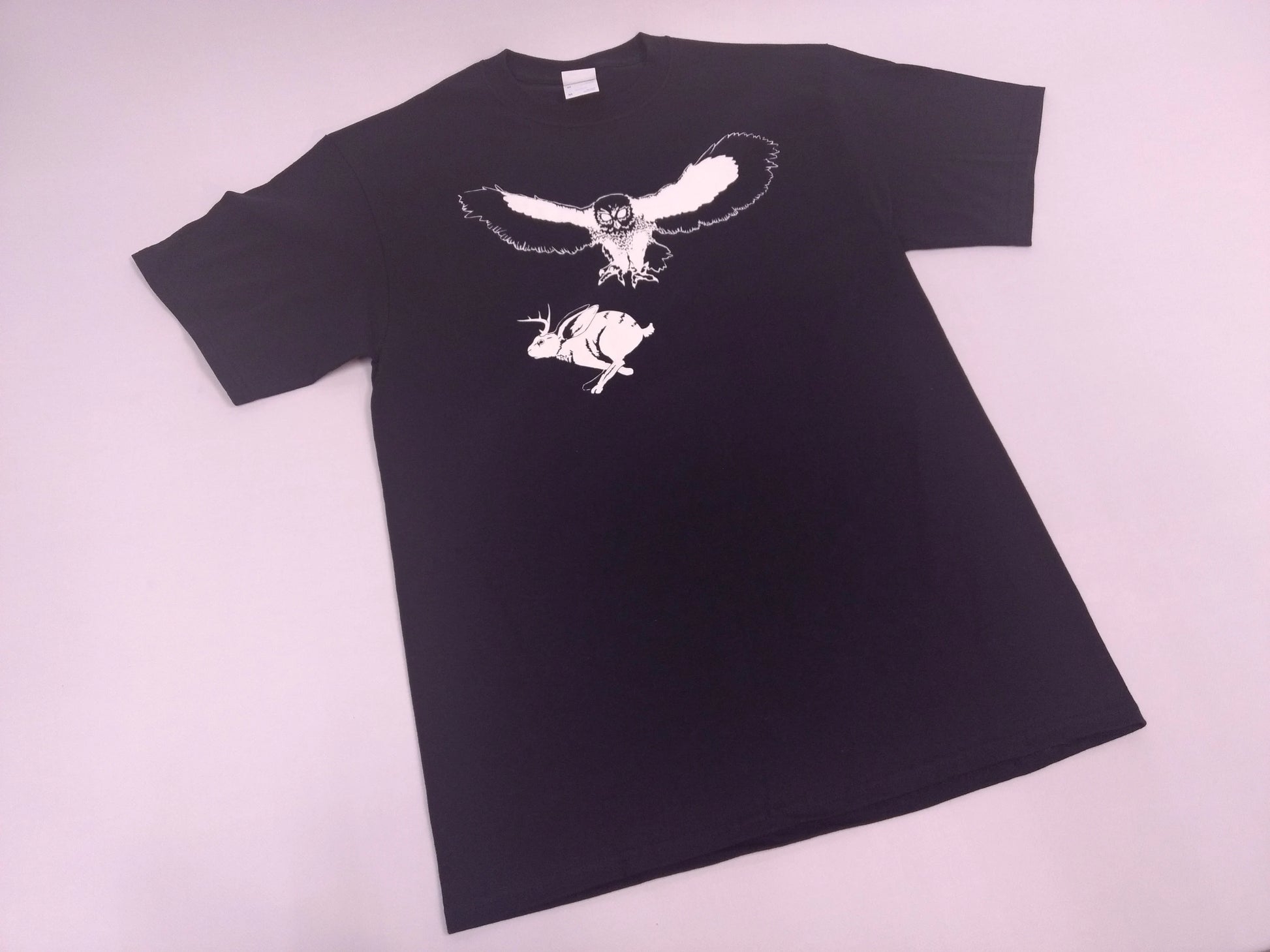 Black t-shirt with white illustration of an owl and a jackalope on a white background