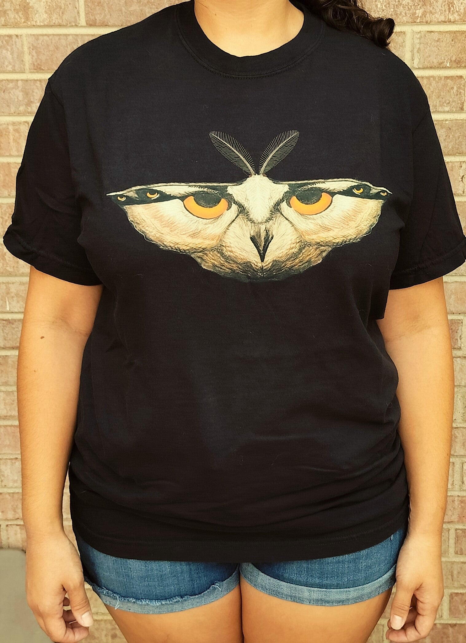Person wearing a black t-shirt with an owl design against a brick wall background